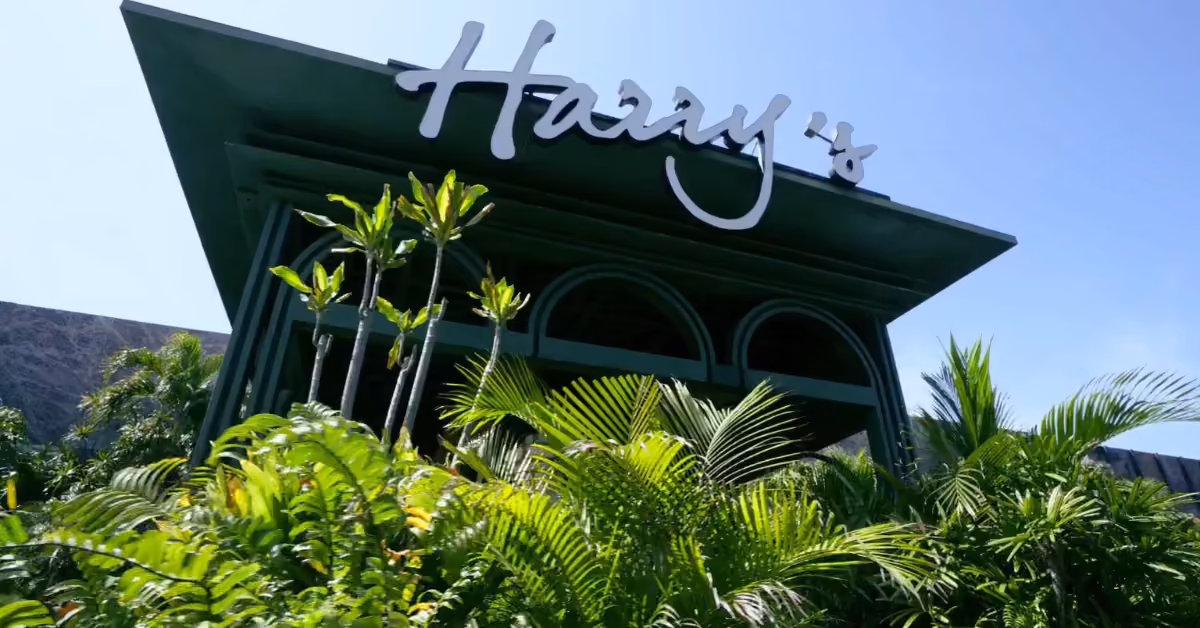 A green building with tropical plants out front and a large Harveys sign stands under a clear blue sky.