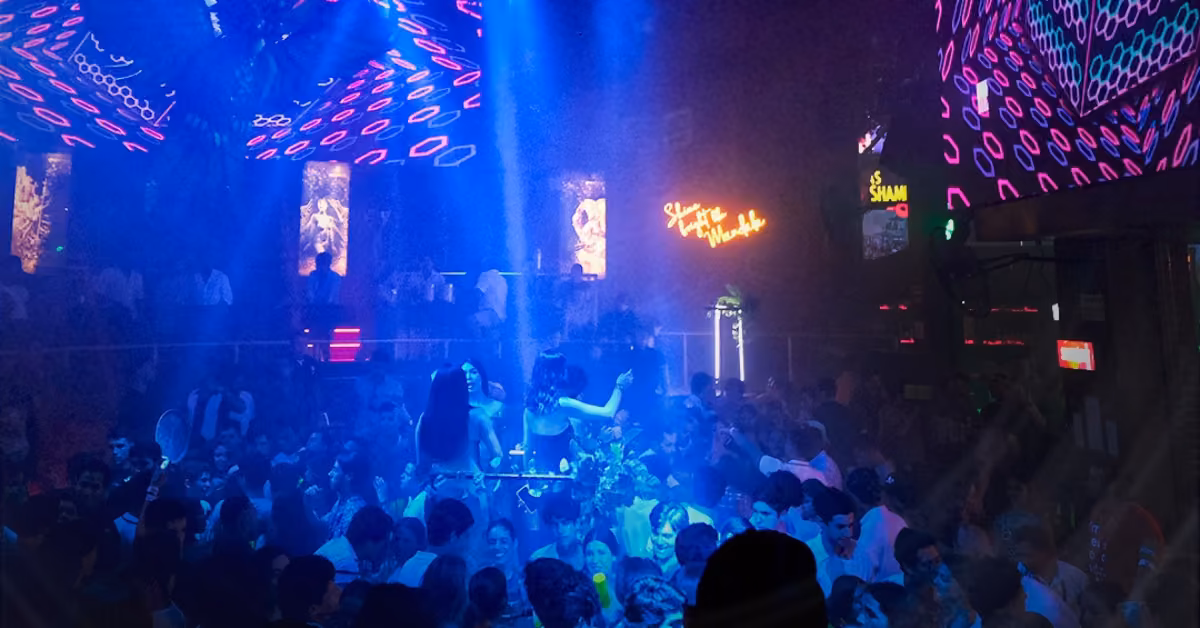 People dance under blue and purple lights at Mandala Night Club, surrounded by neon signs and vibrant LED screens.