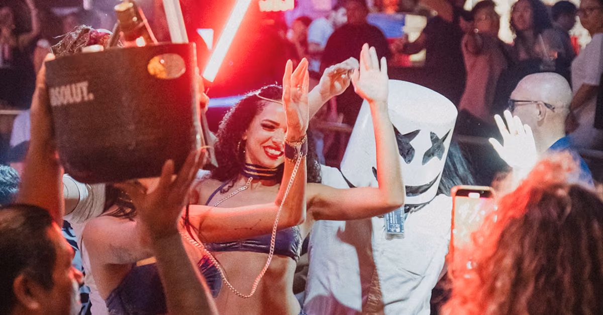People dance and celebrate at Mandala Night Club under colorful lights; a woman smiles, raises her arms, others cheer with drinks.