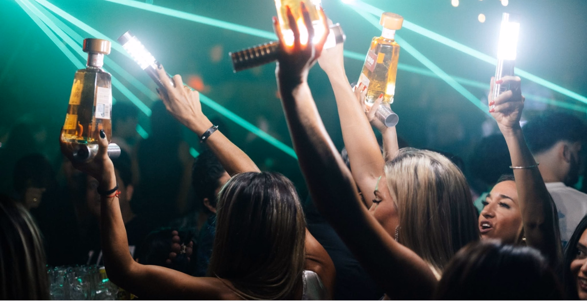 Mun Night Club guests raise bottles with sparklers amid green laser lights and a lively, packed dance floor.
