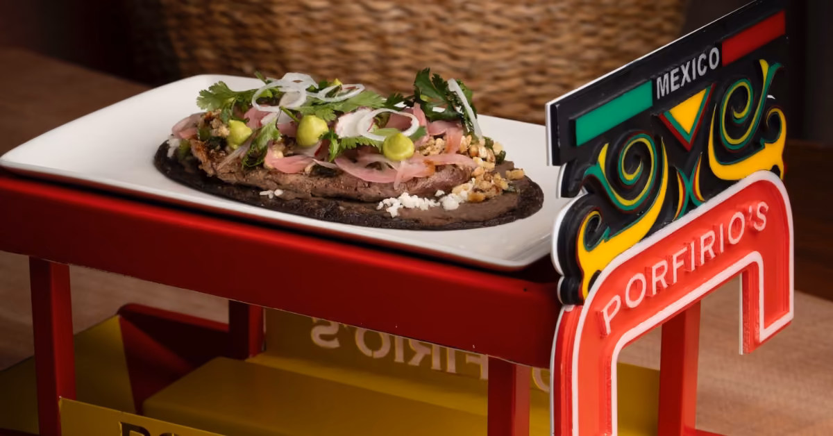 An open-faced taco with sliced meat, onions, cilantro, and green salsa on a colorful tray marked with a Mexico sign.