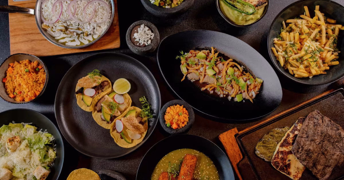 Overhead shot of assorted tacos, rice, pasta, salad, meats, and veggies at Porfirio’s Restaurant on black dinnerware.