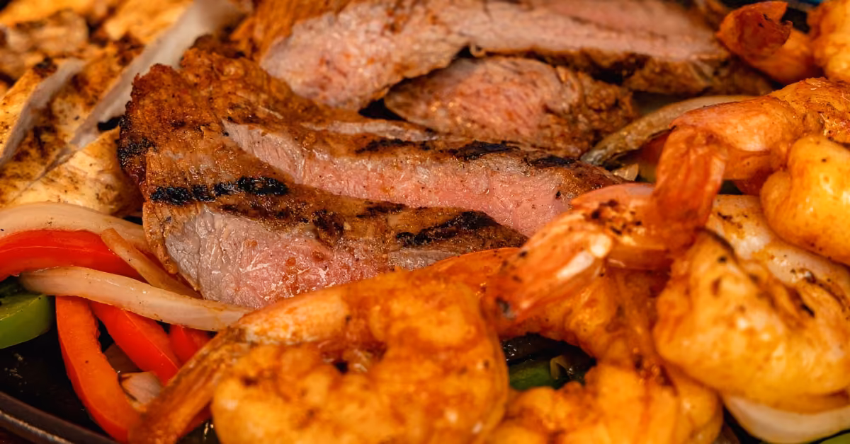 Grilled steak slices, shrimp, onions, and bell peppers served sizzling in a vibrant mixed fajita platter at Señor Frog's.