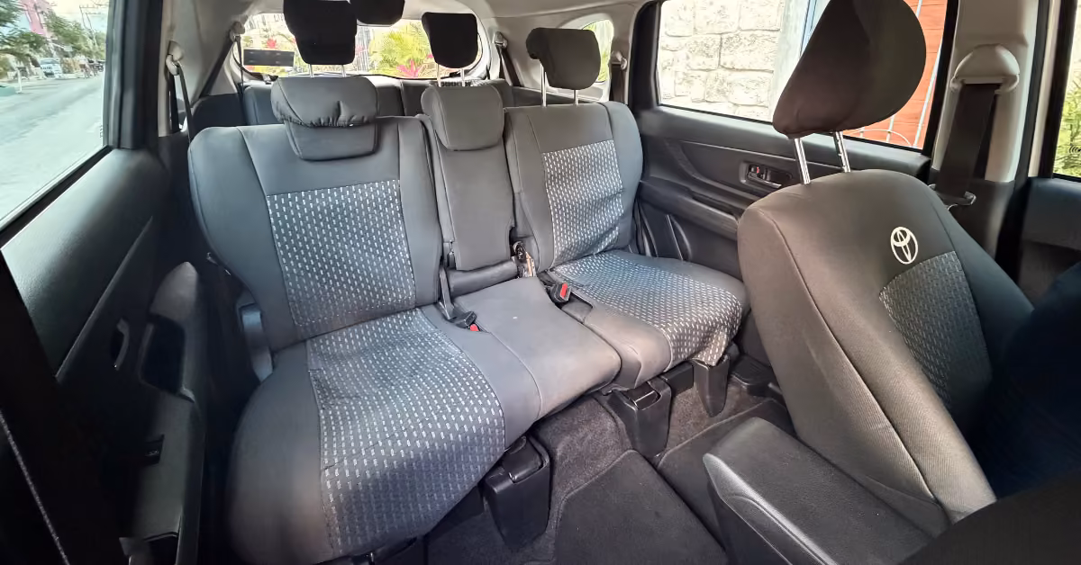 Toyota interior with three rows of black and gray seats, headrests, seatbelt buckles, and sunlight streaming in.