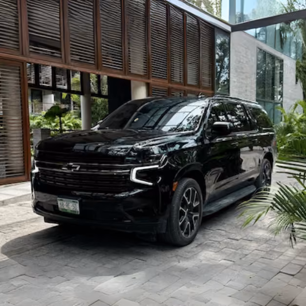 A black Chevrolet SUV is parked on a stone driveway before a modern glass and wood building, surrounded by greenery.