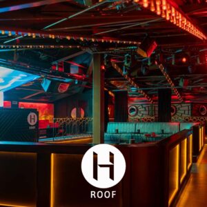 Nightclub interior with red-orange lighting, plush seats, a dance floor, and a prominent H ROOF logo at the front.