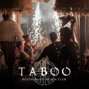 Guests celebrate in a lively restaurant with sparklers as staff in Taboo shirts serve, and the venue name appears at the bottom.